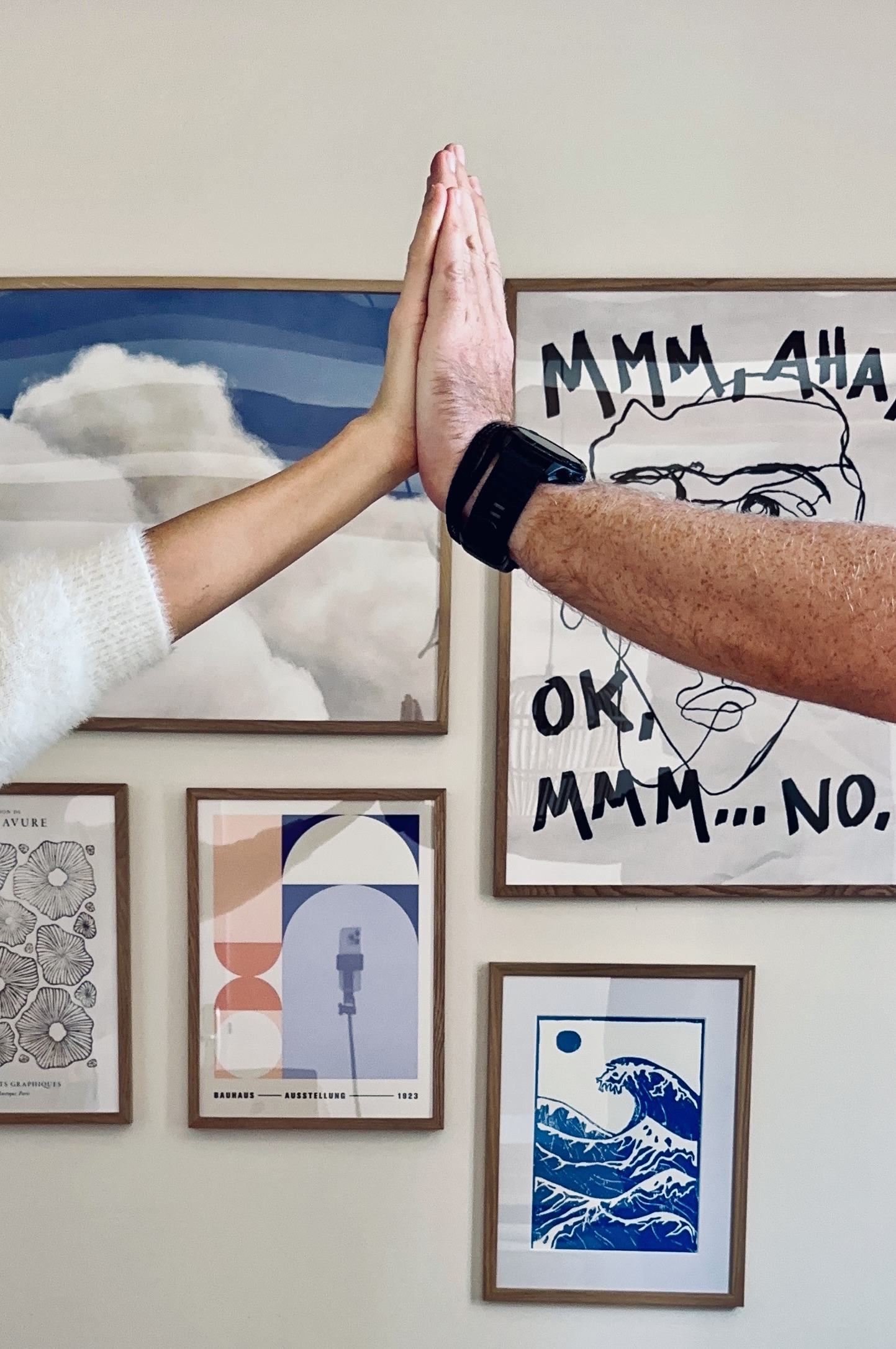 Zwei Personen klatschen zu einem High Five ein. Im Hintergrund sind mehrere gerahmte Kunstwerke an der Wand zu sehen.